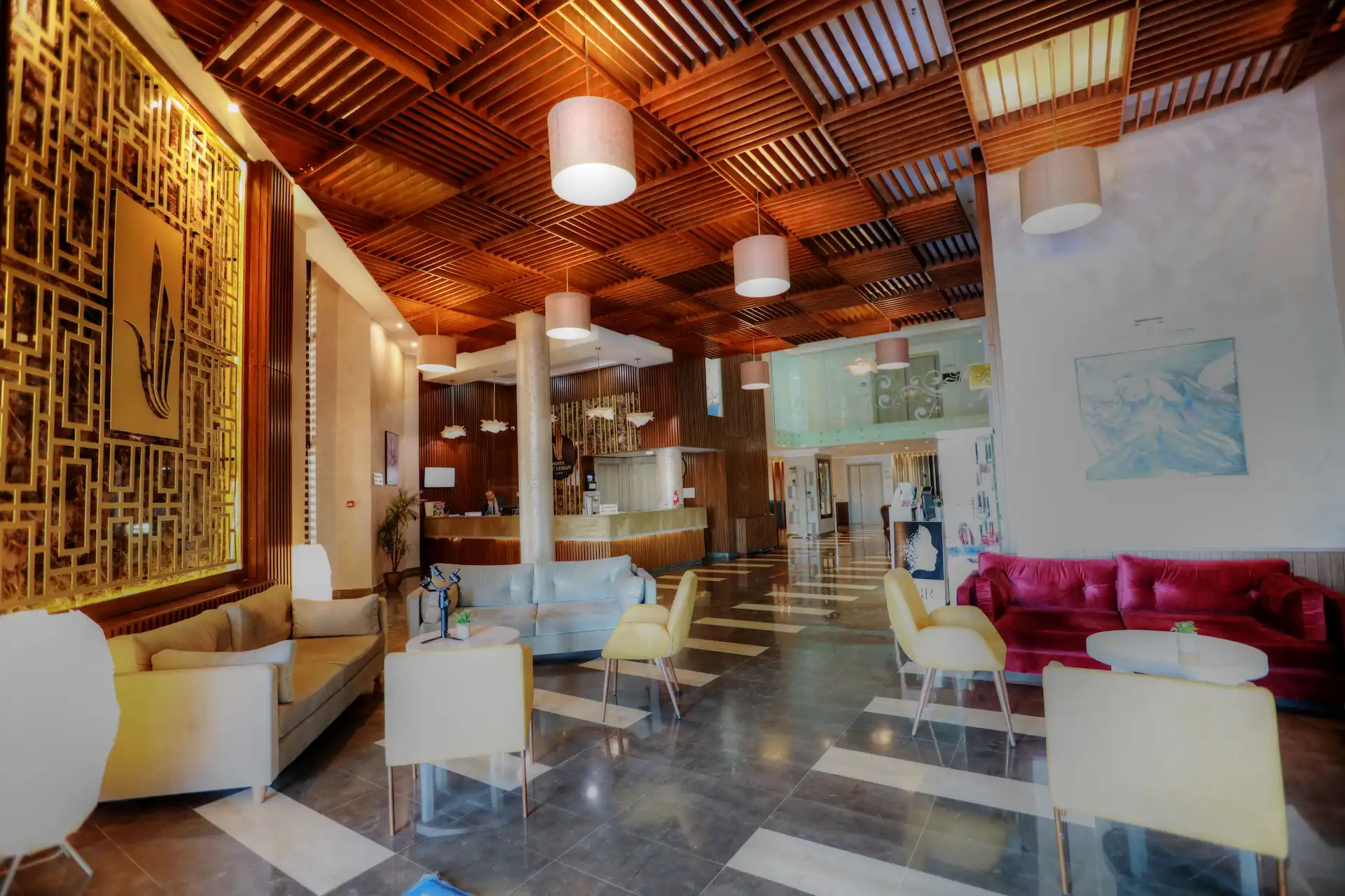 Vue panoramique du lobby moderne et de la réception de l'Hôtel Lac Léman avec canapés en velours, plafond en bois et sol en marbre brillant.