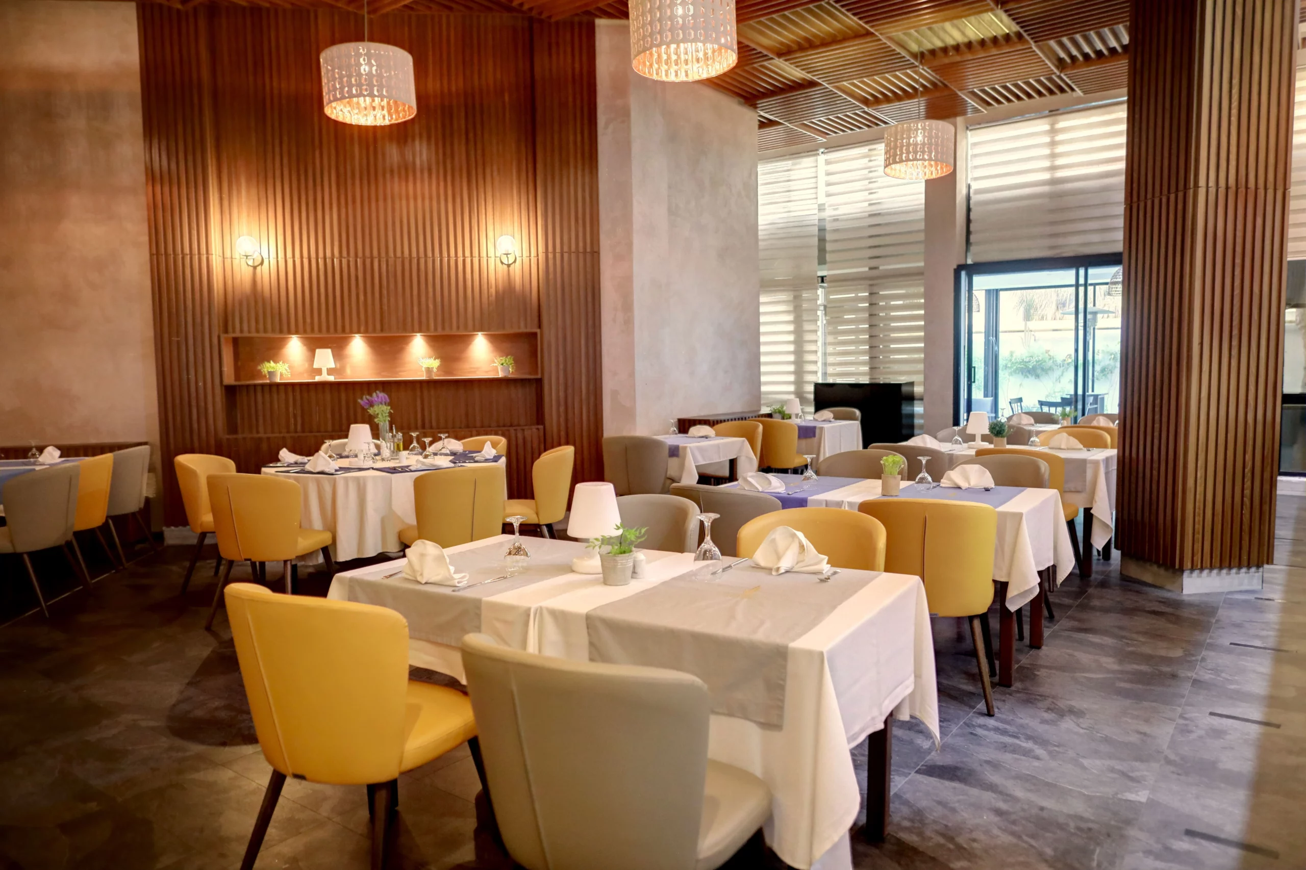 Vue de la salle de restaurant de l'Hôtel Lac Léman avec tables dressées, fauteuils jaunes et gris, et décoration murale en bois élégante.