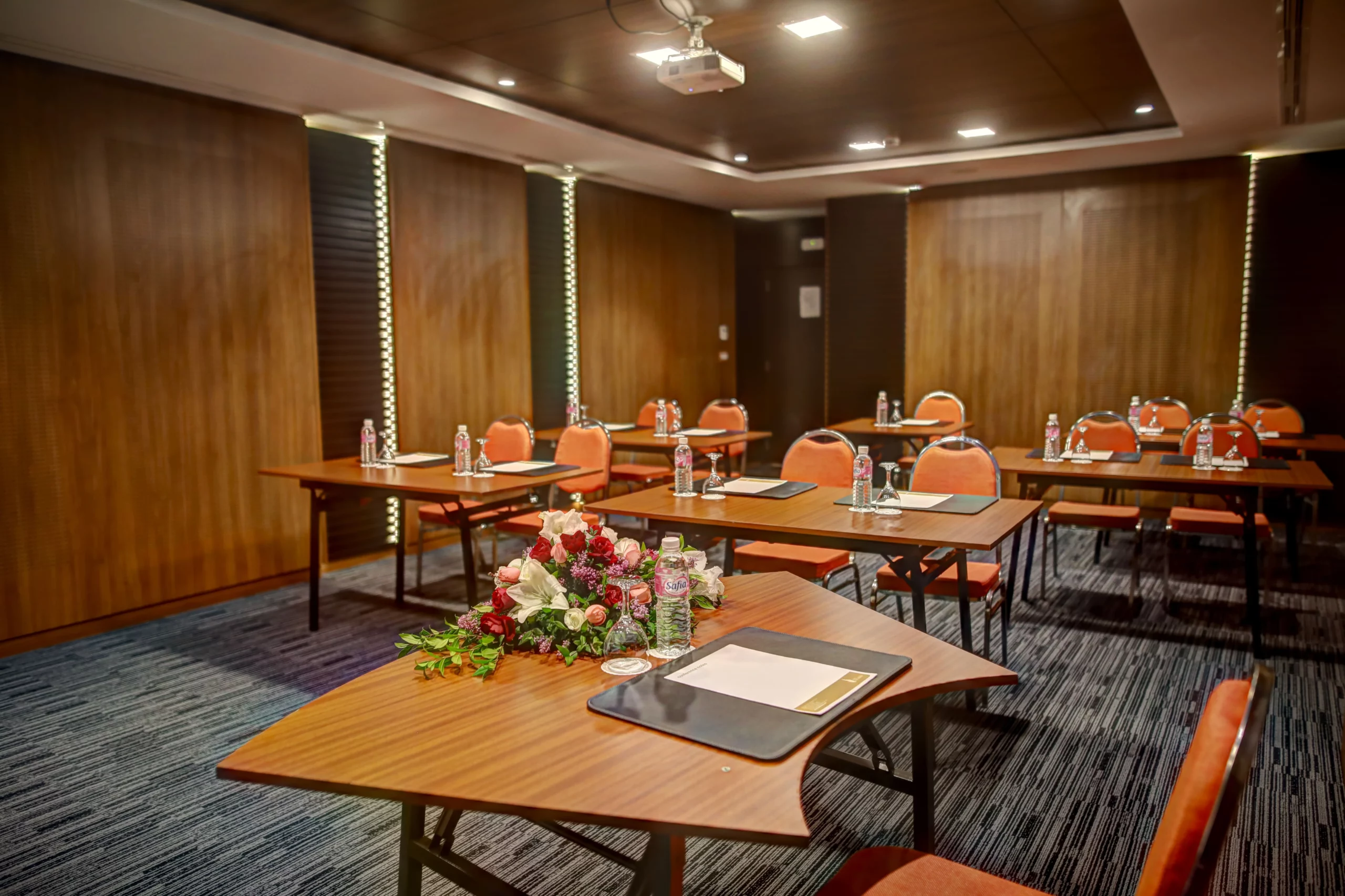 Salle de séminaire moderne de l'Hôtel Lac Léman avec tables en bois disposées en classe, chaises oranges et équipement de conférence.